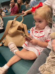 a little girl wearing a santa dress sits on a green bench holding a cell phone