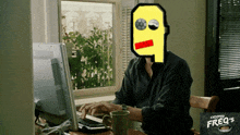 a man sits at a desk with a computer and a cup of coffee with a cartoon face on his face
