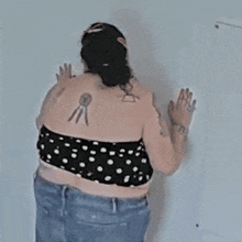 a woman with a tattoo on her back is standing next to a wall .