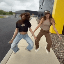 two girls are dancing on a sidewalk with one wearing a hat that says a on it