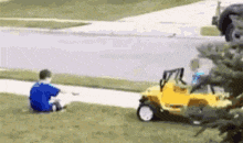a boy is sitting on the grass next to a toy car