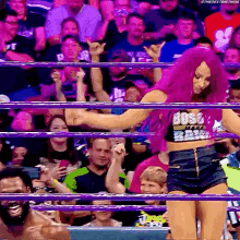 a woman with purple hair is standing in a wrestling ring with her hands in the air .