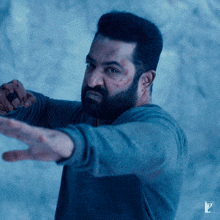 a man with a beard is wearing a blue shirt and pointing