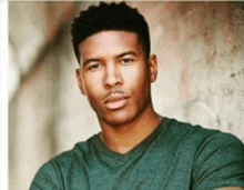 a young man in a green t-shirt is standing in front of a wall .