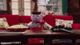 a stuffed animal is sitting on a red couch looking at a cell phone