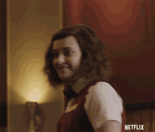 a woman in a vest and bow tie is smiling and says " what "