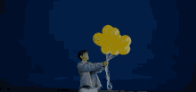 a man is holding a bunch of yellow balloons in his hand
