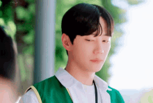 a young man wearing a green vest and a white shirt is looking down at something .