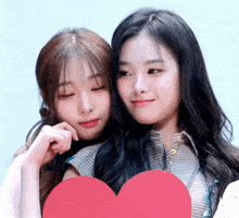 two girls are hugging each other and holding a heart