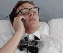 a man with glasses is laying on a couch talking on a phone
