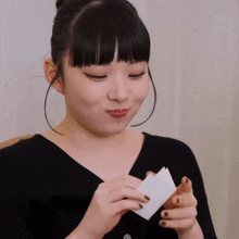 a woman in a black shirt holds a piece of paper in her hand