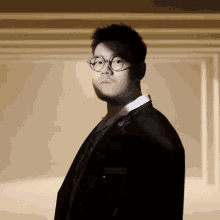 a man wearing glasses and a suit stands in a dark room