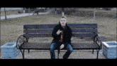 a young man sits on a wooden bench in a park holding a cell phone