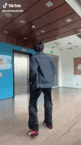 a man in a denim jacket is standing in front of an elevator and a sign that says exit on it