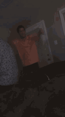 a man in an orange shirt stands in a dark room