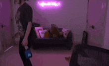 a woman is standing in front of a couch with a purple neon sign behind her .