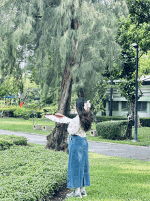 a woman in a blue skirt is standing in front of a tree in a park