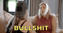 two women are sitting on a couch and one has a bandage on her head and the word bullshit is above her