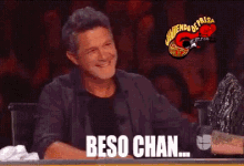 a man covering his face with his hand while sitting at a table with the words beso chan written on it