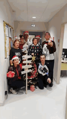 a group of people posing in front of a christmas tree with one wearing a sweater that says ho