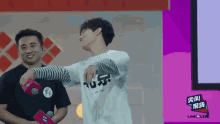 a man in a black shirt stands next to a man in a white shirt that says ' live 4 live ' on it