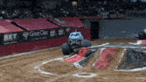 a monster truck is driving down a dirt track in front of a bkt banner