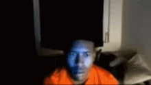 a man in an orange shirt is sitting in front of a screen