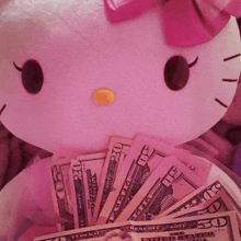 a stuffed hello kitty is holding a fan of twenty and fifty dollar bills