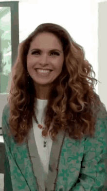 a woman with long curly hair is smiling and wearing a green jacket