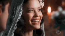 a woman wearing a white lace veil smiles while looking at a man