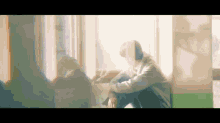 a man is sitting on the floor in front of a window with his head down .