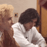two men are sitting next to each other and one has a microphone in his shirt