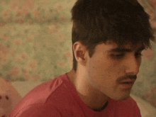 a young man with a mustache is sitting on a bed .
