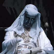 a man in a white robe with a blue mask on his face is reading a book