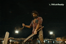 a man with a beard is holding a cricket bat in front of a sign that says " 7wickreddy "