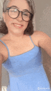 a woman wearing glasses and a blue tank top takes a selfie
