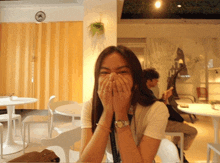 a woman covering her mouth with her hands in a room with a clock on the wall