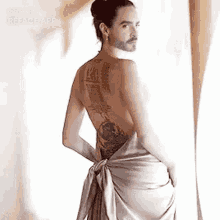 a man with a beard and a tattoo on his back is wearing a white dress .