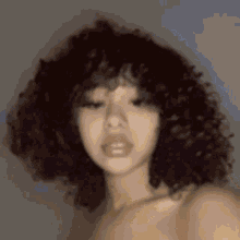 a woman with curly hair is taking a selfie without a shirt .