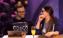 a man and a woman are sitting at a table with a glass of orange juice and a tablet .