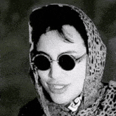 a black and white photo of a woman wearing sunglasses and a leopard print scarf .