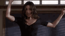 a woman in a black shirt is dancing with her arms outstretched in a room .