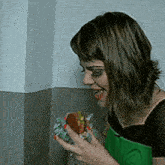 a woman in a green apron is holding a sandwich