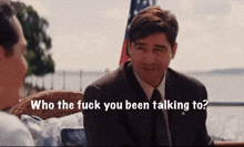 a man in a suit and tie is talking to another man in a chair who the fuck you been talking to