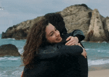 a man and a woman hugging on a beach with the tv logo in the background