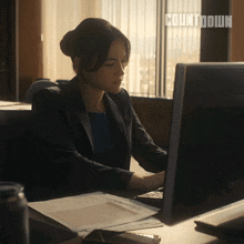 a woman sits at a desk in front of a computer with countdown written on the screen