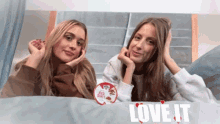 two women laying on a bed with the words love it on the bottom right