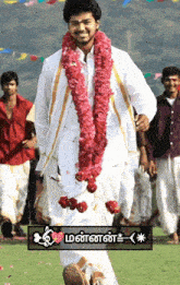 a man wearing a garland of pink flowers is walking in a field with other men