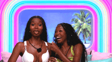 two women are sitting on a couch with a palm tree in the background .