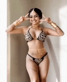 a woman in a bikini is standing in front of a window making a peace sign .